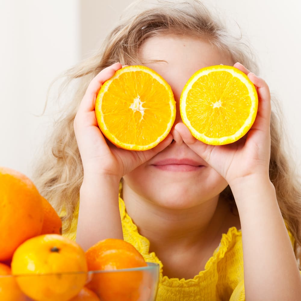 A little girl holds bright orange slices over her eyes