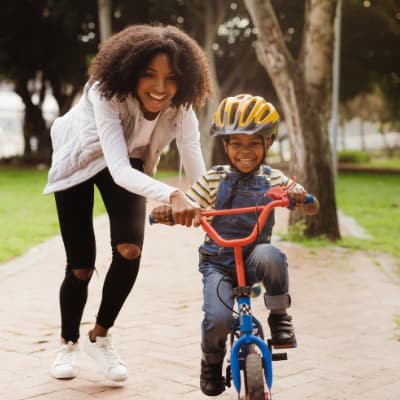 A Black mother and son, out at the park riding a bike