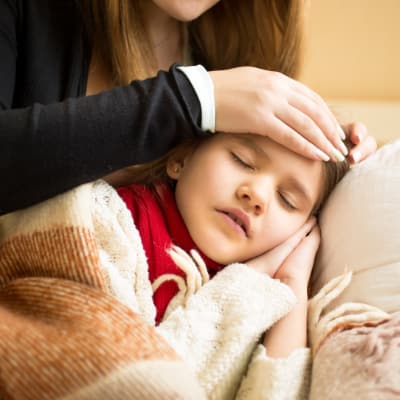 A mother feels her daughter's forehead, checking for fever